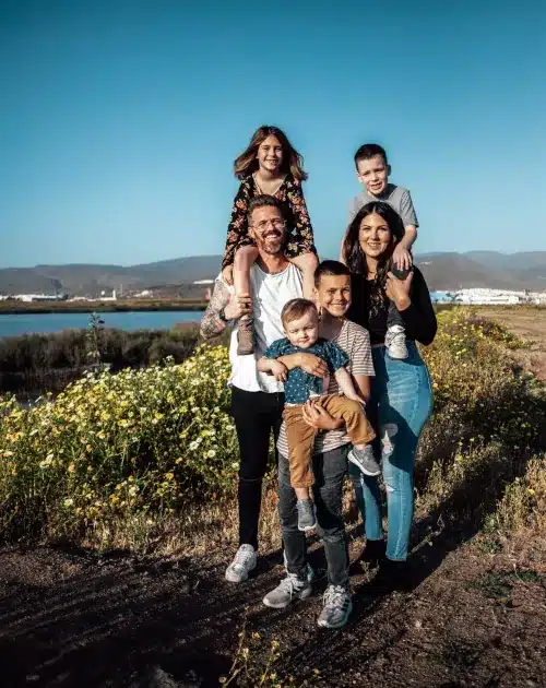 Buyers Scout International Buyers Agent Brisbane Family of six with four small children. Situated with the beach in the background. Two of the children are on the shoulders of each parent.